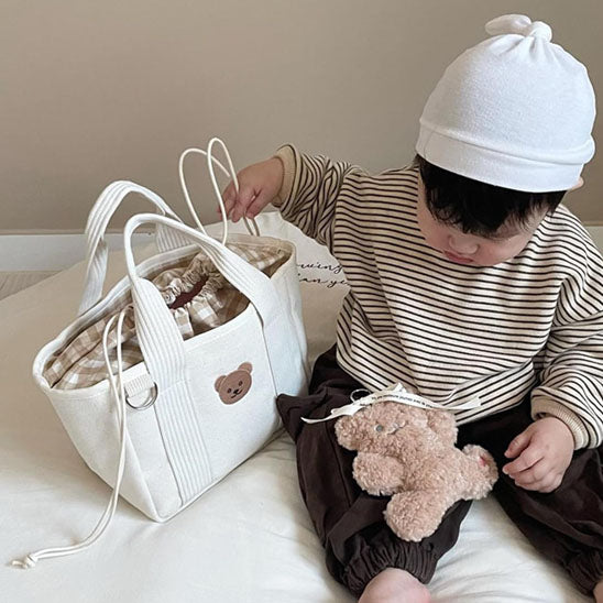 assis sur le lit bébé tient un sac à langer maternité pour bebe et maman 