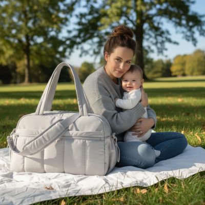 maman assise sur avec bebe dans un park naturel avec un sac a langer poser a cote